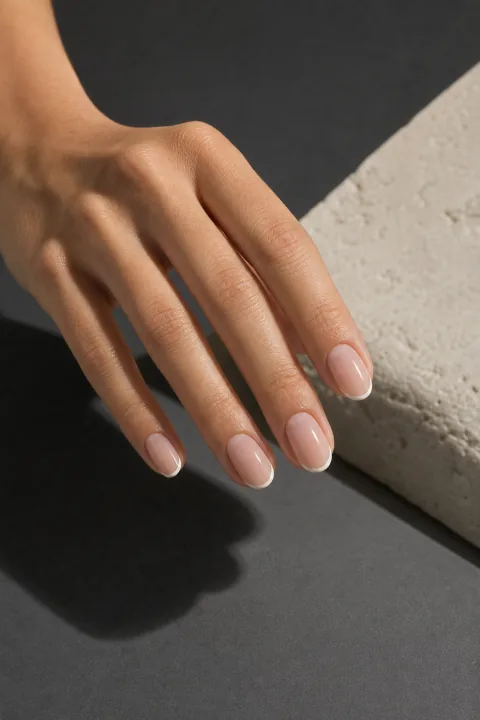 Mão com unhas ovais e francesinha branca fina sobre base nude