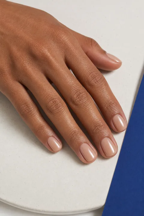 Mão com unhas curtas quadradas em gel nude translúcido junto a detalhe azul